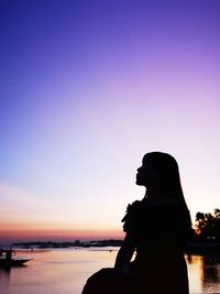 Silhouette woman standing by sea against dramatic sky during sunset