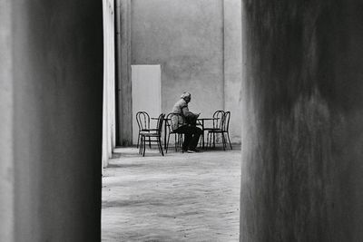 Side view of man sitting on chair against wall