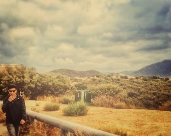 Person standing on grassy field against cloudy sky