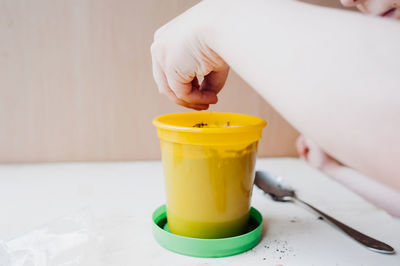 Close-up of hand holding yellow cup on table