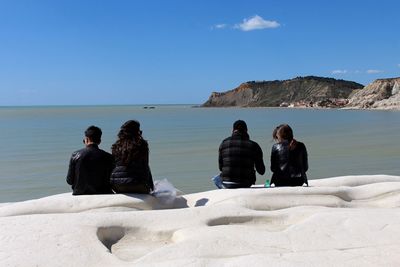 Rear view of people sitting on beach against clear sky