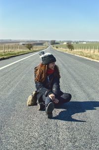 Portrait of woman sitting on road against clear sky