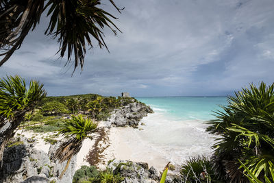 Scenic view of rock formation by sea at beach against cloudy sky