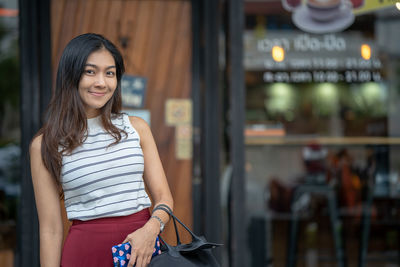 Portrait of smiling mid adult woman standing against cafe in city