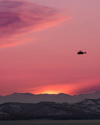 Airplane flying over mountains against sky during sunset