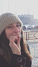 Portrait of young woman smoking weed on snowy field in city