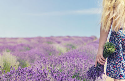 Rear view of woman standing on purple flowering plants on field against sky