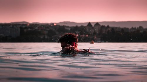 Woman swimming in pool against sky during sunset