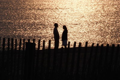 Silhouette couple standing at beach during sunset