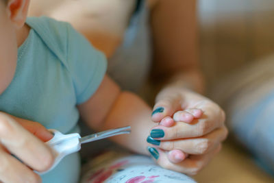 Cropped image of mother cutting toddler fingernails with scissors