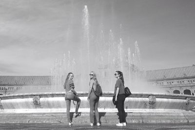 Full length of friends standing on fountain against sky