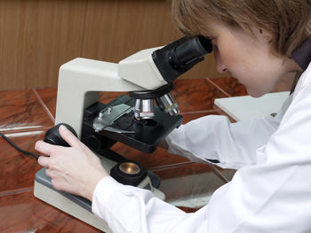 Side view of scientist using microscope on table