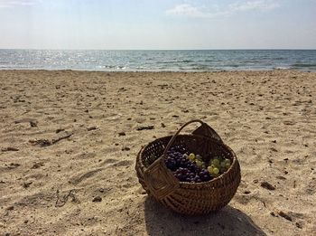 Wicker basket on sand at beach against sky