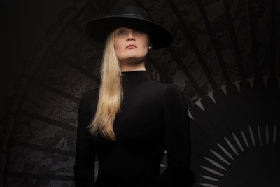 Young woman looking away while standing against black background