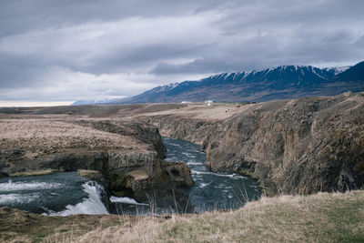 Scenic view of waterfall and landscape against cloudy sky