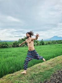 Shirtless man running on field against sky