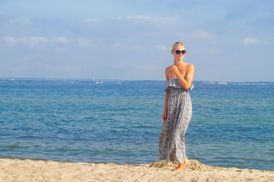 Full length of young woman standing at beach against sky