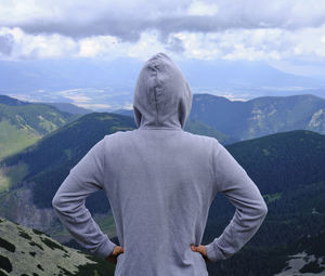 A boy in a sweatshirt from behind on top of a hill enjoys the view