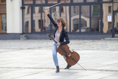 Portrait of smiling woman holding violin while dancing on street