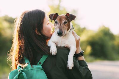A young girl in a jacket with a green backpack on her shoulders holds a dog in her arms and hugs her