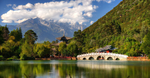 Arch bridge over lake by trees against sky