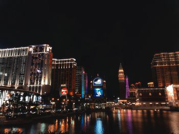 Illuminated buildings by river against sky at night