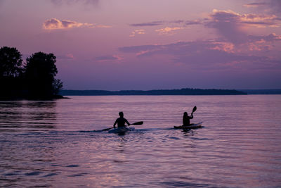 Silhouette people on sea against sky during sunset