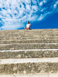 Low angle view of woman sitting on staircase against sky