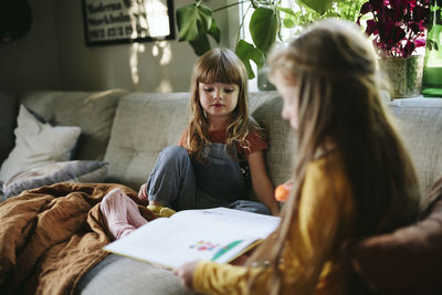 Sisters reading book on sofa