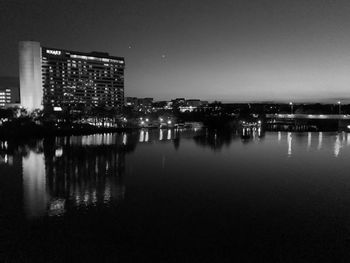 Illuminated buildings by river against sky in city at night