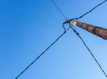 Low angle view of electricity pylon against clear blue sky