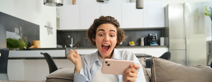 Portrait of young woman using mobile phone while sitting at home