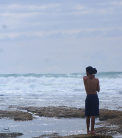 Rear view of man standing on beach against sky