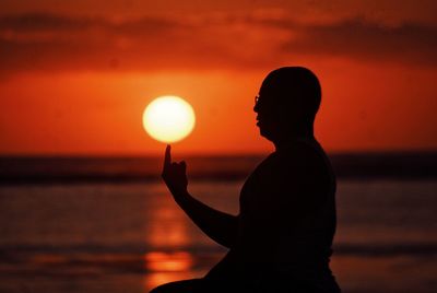 Optical illusion of man holding sun on finger against sky during sunset