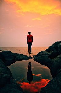 Rear view of silhouette man standing on rock at beach