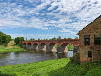 Arch bridge over river by buildings against sky