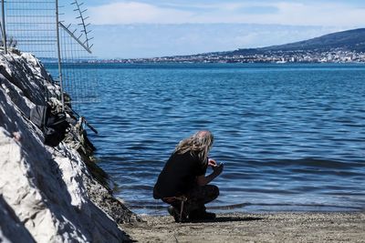Woman sitting on shore by sea against sky