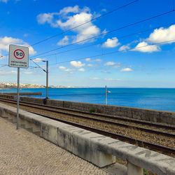 Road sign by sea against sky