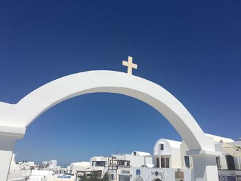 Cross on whitewashed arch against clear blue sky