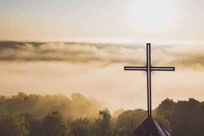 Cross overlooking trees covered with clouds