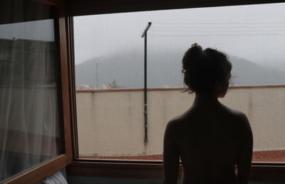 Rear view of shirtless girl against window at home