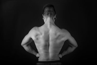 Rear view of shirtless man standing against black background