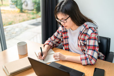 Young woman using mobile phone while sitting on table