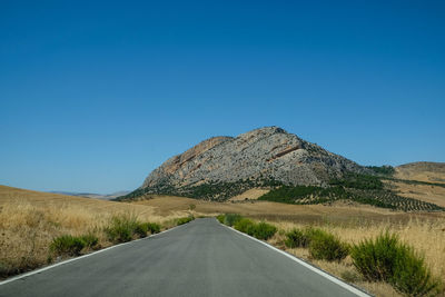 Road leading towards mountain against clear blue sky