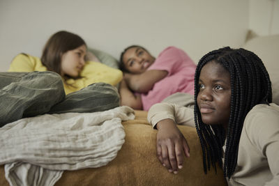 Contemplative teenage girl with braided hair by female friends lying in bedroom