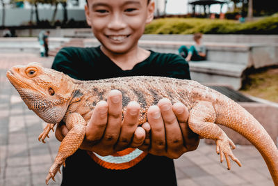 Smiling boy holding lizard while standing outdoors