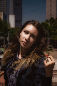 Portrait of beautiful young woman standing against buildings in city