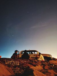 People sitting by car against sky at night