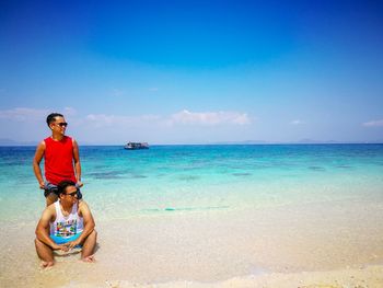 Man sitting at beach against blue sky