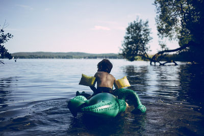 Rear view of woman sitting in lake against sky